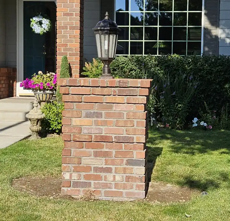 Black coach lamp on a brick pillar among garden plantings, an exterior lighting job wired by Castle