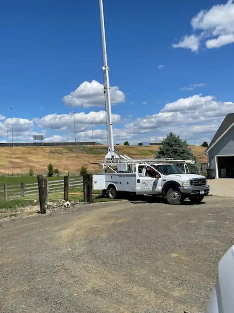 Castle boom truck with its mast raised in a rural driveway under a blue sky