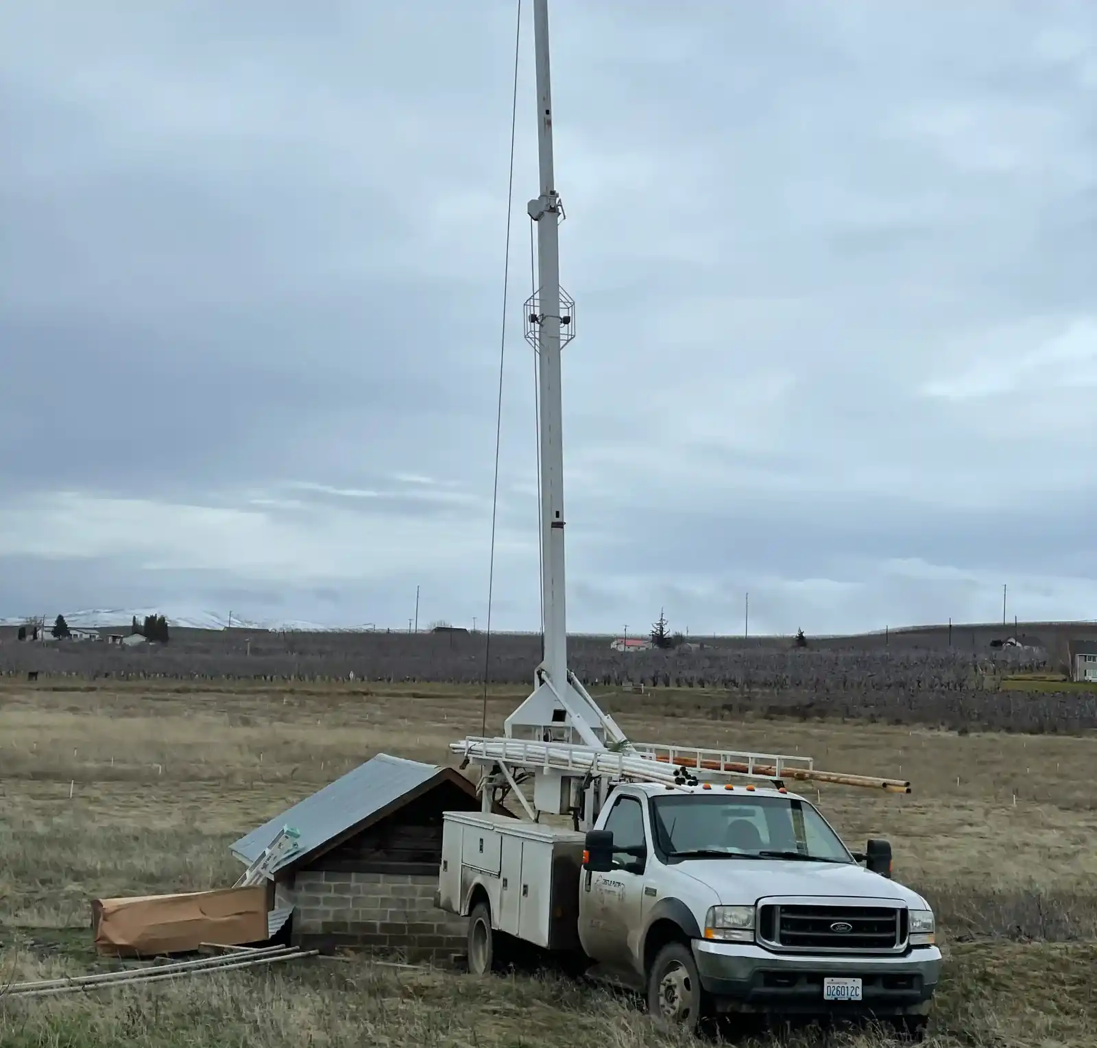 Castle Pump & Electric hoist truck with its mast raised over a concrete block pump house in an open field