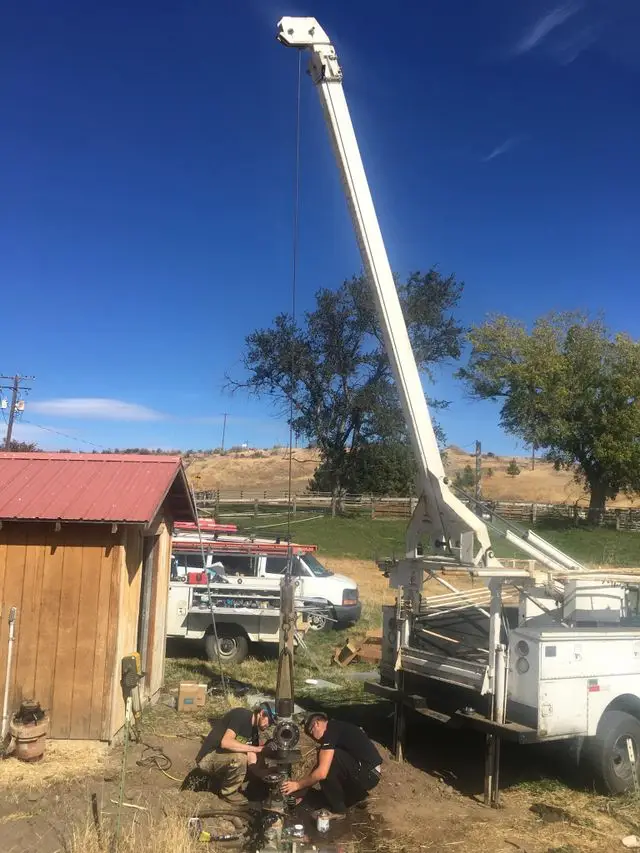 Two Castle crew members kneeling at a wellhead under the raised boom, pulling a pump